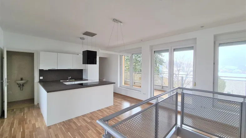 Heller offener Wohn- und Essbereich mit integrierter Küche, Parkettboden und Zugang zum Balkon.