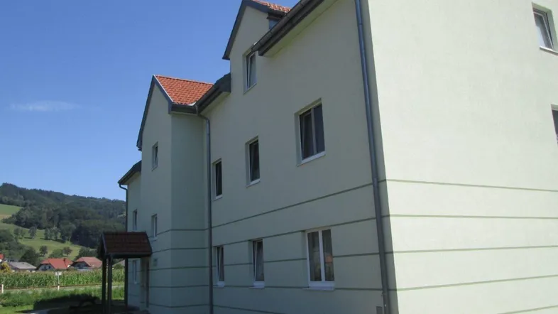 Ansicht des Mehrfamilienhauses mit hellgrüner Fassade und rotem Ziegeldach in ländlicher Umgebung.