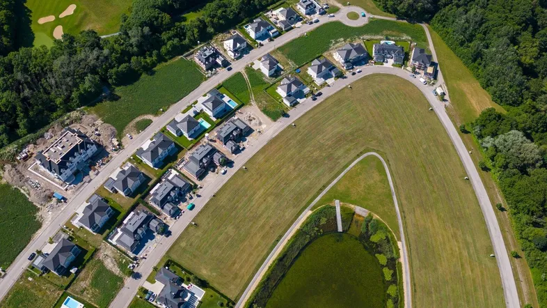 Luftaufnahme einer Wohnsiedlung mit Häusern, Grünflächen, einem Golfplatz und einem Teich.