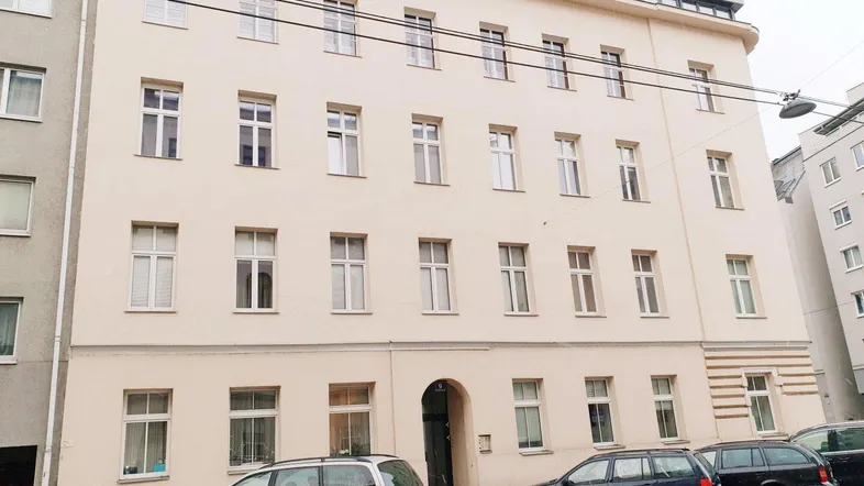 Die Fassade eines Mehrfamilienhauses mit vielen Fenstern und parkenden Autos auf der Straße.