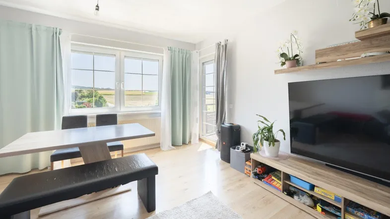 Heller Wohn- und Essbereich mit Holzboden, großen Fenstern und Zugang zum Balkon.