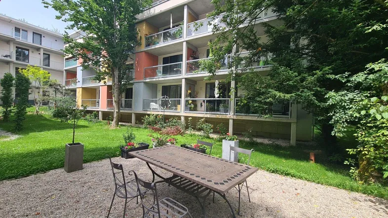 Außenbereich mit Kiesterrasse und Gartenmöbeln vor einem modernen Wohngebäude mit Balkonen.