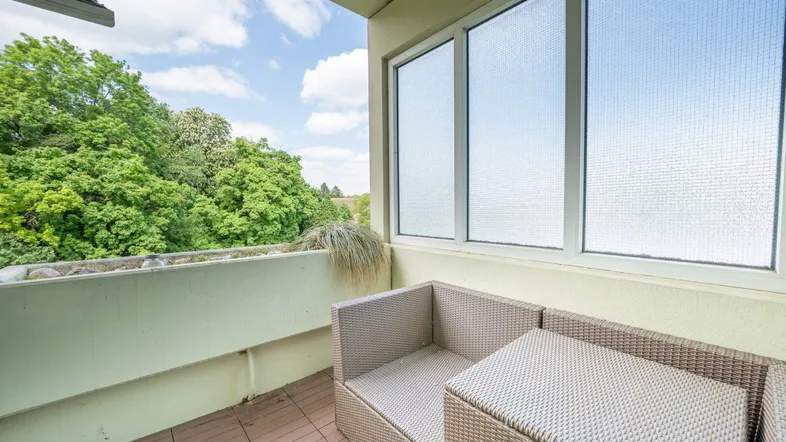 Möblierter Balkon mit Blick ins Grüne und bequemen Sitzgelegenheiten unter blauem Himmel.