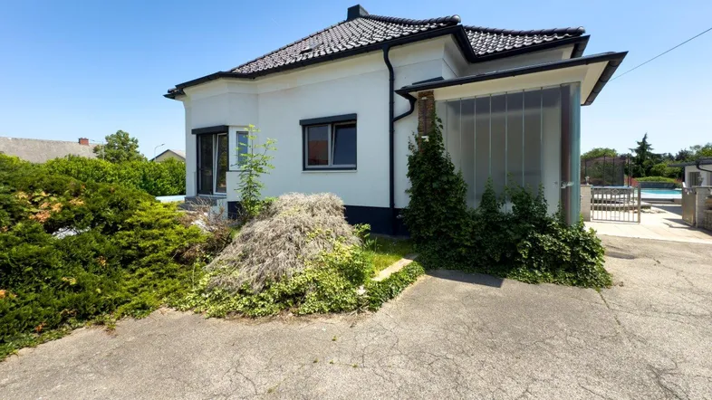 Weißes Einfamilienhaus mit dunklem Dach, umgeben von Grünflächen und einer gepflasterten Auffahrt.