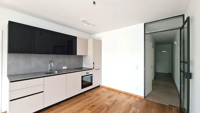 Moderne Einbauküche mit schwarzen Oberschränken und hellem Holzfußboden, offen zum Flur.