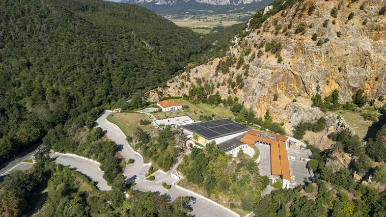 Luftaufnahme eines weitläufigen Anwesens in einer bergigen, grünen Landschaft mit mehreren Gebäuden.