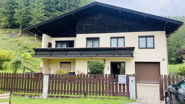Traditionelles Haus mit Balkon, Garage und umgeben von grünen Wäldern.