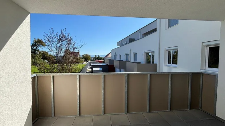Heller Balkon mit Fliesenboden und Blick auf die umliegenden Neubauten und Grünflächen.