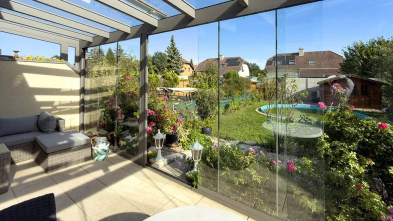 Verglaste Terrasse mit Sitzgelegenheiten und Blick auf den Garten mit Pool.