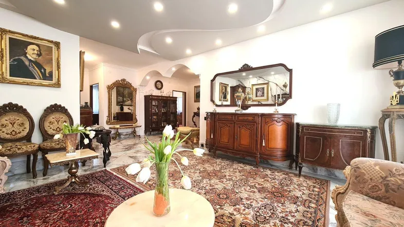 Elegantes Wohnzimmer mit klassischen Möbeln, Teppichen und dekorativer Deckenbeleuchtung in einem gepflegten Ambiente.