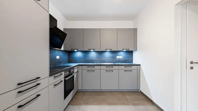Moderne Einbauküche in Grau mit dunkler Arbeitsplatte, integriertem Backofen und Dunstabzugshaube.