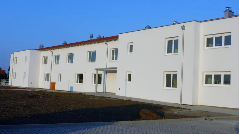 Neues Wohngebäude mit weißer Fassade, vielen Fenstern und noch unfertigem Außenbereich.
