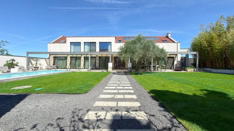 Großzügiger Gartenbereich mit Rasenfläche, Pool und modernem Wohnhaus im Hintergrund unter blauem Himmel.