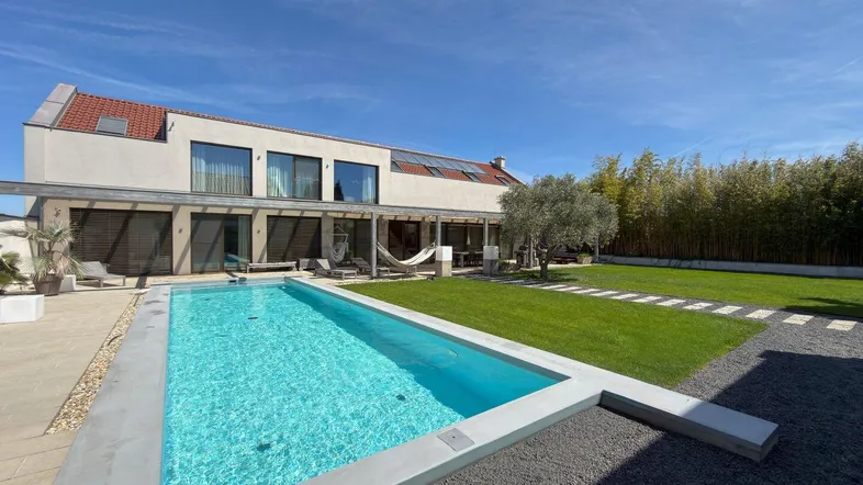Modernes Haus mit großem Garten, Swimmingpool und Sonnenterrasse unter blauem Himmel.