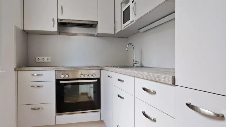 Moderne, kompakte Küche mit weißen Schränken, Holzboden und integrierten Geräten.