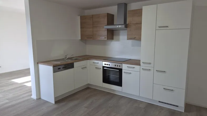 Moderne Einbauküche mit weißen Fronten, Holzdetails, integrierten Geräten und Laminatboden.