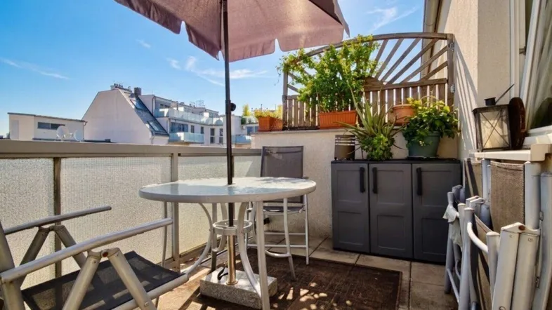 Heller Balkon mit Sitzgelegenheiten, Sonnenschirm und Blick auf die umliegenden Gebäude.