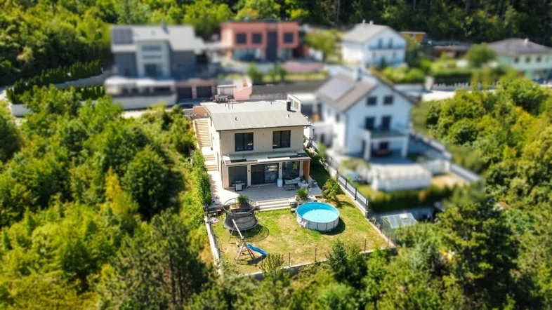 Luftaufnahme eines modernen Hauses mit Garten, Pool und Trampolin, umgeben von viel Grün.