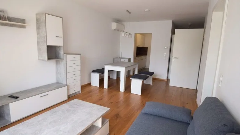 Helles Wohn- und Esszimmer mit Holzboden, modernem Mobiliar und Zugang zur Küche.