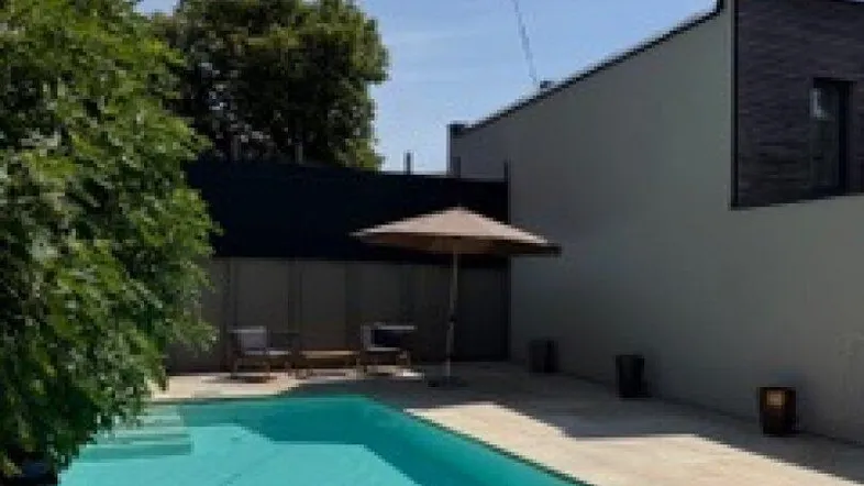 Großer Außenpool mit gepflasterter Terrasse und moderner Gebäudearchitektur an einem sonnigen Tag.