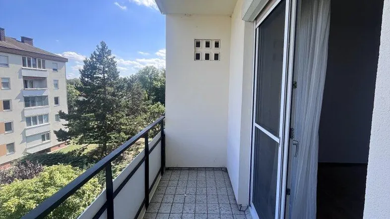 Heller Balkon mit Fliesenboden und Blick auf die umliegenden Gebäude und Bäume.