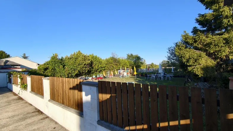 Gepflegter Gartenbereich mit Holzzaun, Rasenfläche und Sitzgelegenheiten unter blauem Himmel.