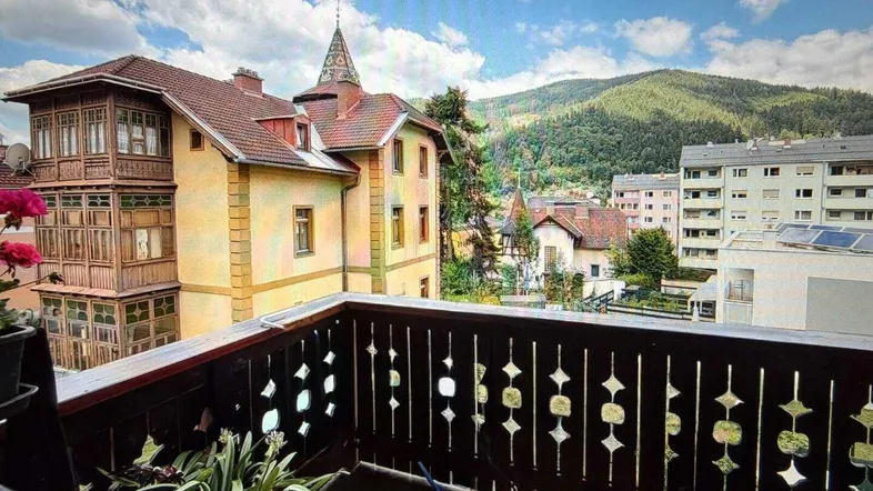 Balkon mit Holzbalkon und Blick auf historische Gebäude sowie die umliegende Berglandschaft.