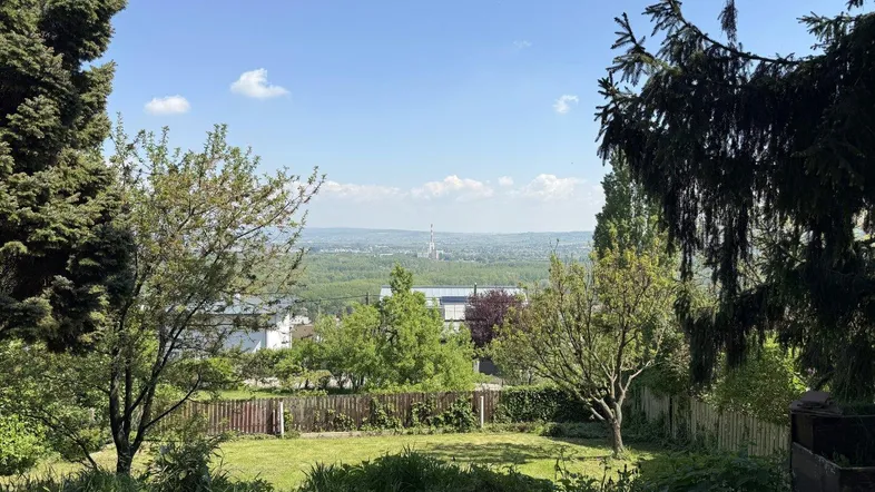 Gartenbereich mit weitem Blick über die Landschaft und viel Grün unter blauem Himmel.