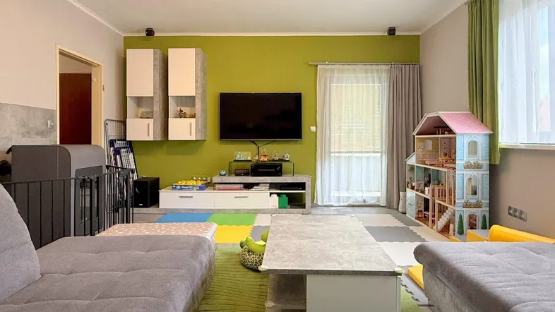 Helles Wohnzimmer mit Spielbereich, grüner Akzentwand und modernem Sofa.