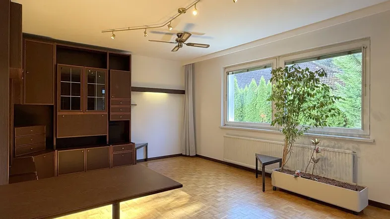 Helles Wohnzimmer mit Parkettboden, großem Fenster und integriertem Regal.