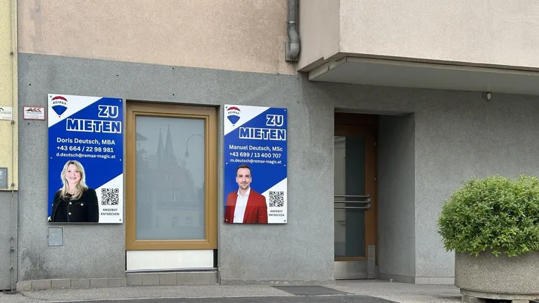 Gebäudefassade mit zwei 'Zu vermieten'-Schildern und einem kleinen Busch in einem Topf.