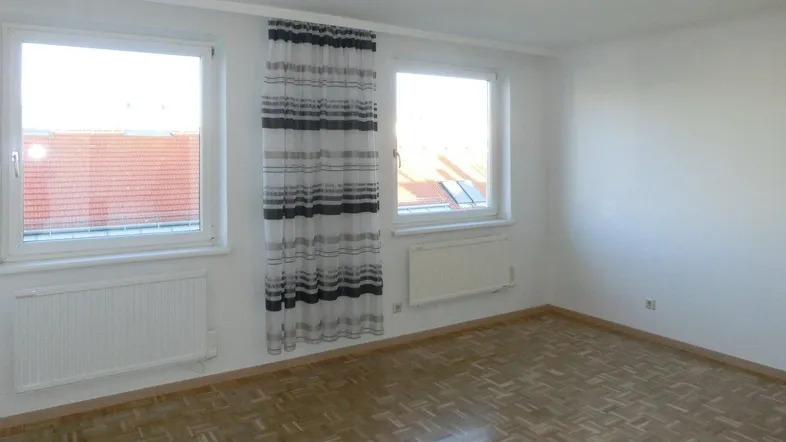 Helles Zimmer mit zwei Fenstern, Parkettboden und Heizkörpern, bereit zur individuellen Gestaltung.