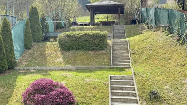 Gestufter Gartenbereich mit Steintreppen, üppigem Grün und einem Holzpavillon im oberen Bereich.