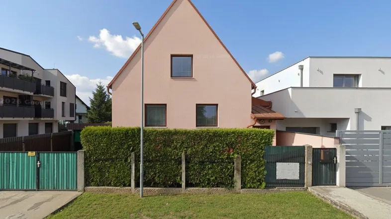 Einfamilienhaus mit rosafarbener Fassade und gepflegter Hecke im Vorgarten.
