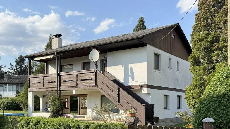 Traditionelles Haus mit weißer Fassade, Holzbalkon und Außentreppe unter blauem Himmel.