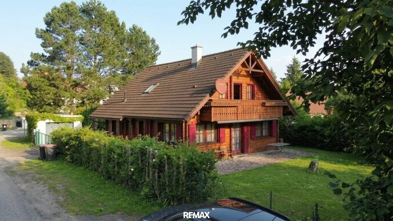 Blockhaus mit traditioneller Holzfassade und gepflegtem Vorgarten unter blauem Himmel.
