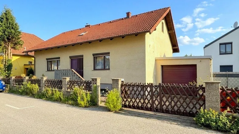 Einfamilienhaus mit gelber Fassade, rotem Ziegeldach und Vorgarten in sonniger Lage.
