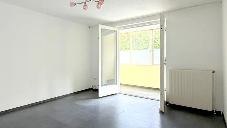 Helles Zimmer mit dunklem Fliesenboden und Zugang zu einem verglasten Balkon, ideal als Wohnbereich.