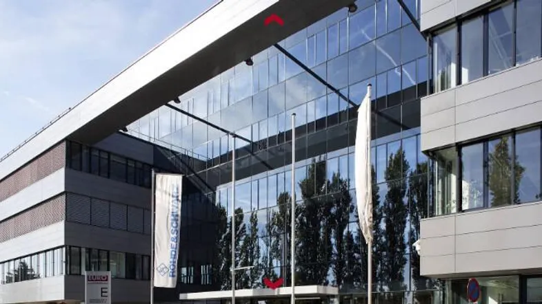 Modernes Bürogebäude mit beeindruckender Glasfassade und klaren architektonischen Linien unter blauem Himmel.