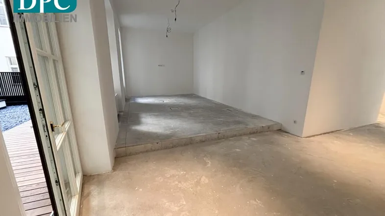 Leerer Raum mit Rohbetonboden und Zugang zu einem Außenbereich, bereit für den Ausbau.