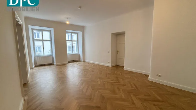 Geräumiges Wohnzimmer mit Fischgrätparkett, hohen Decken und großen Fenstern, bereit zur Einrichtung.
