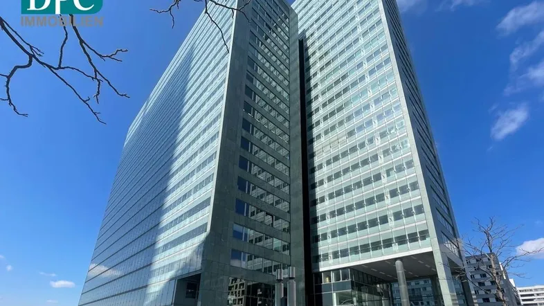 Modernes Hochhaus mit beeindruckender Glasfassade unter blauem Himmel, umgeben von städtischer Architektur.