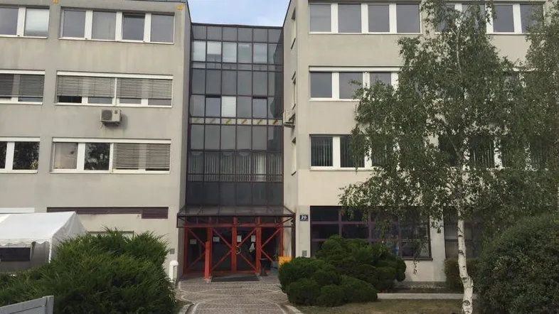 Gebäudefassade eines modernen Bürogebäudes mit Glasfront und Bäumen im Vordergrund.
