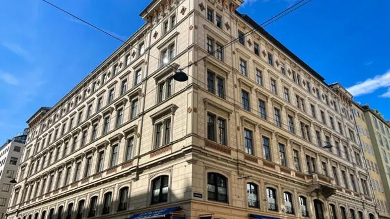 Historisches Eckgebäude mit reich verzierter Fassade und Geschäften im Erdgeschoss unter blauem Himmel.