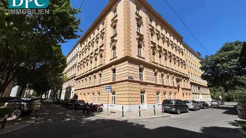 Historisches Eckgebäude mit reich verzierter Fassade und vielen Fenstern an einem sonnigen Tag.