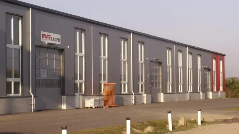 Modernes Industriegebäude mit grauer Fassade, vielen hohen Fenstern und einem roten Akzentbereich.