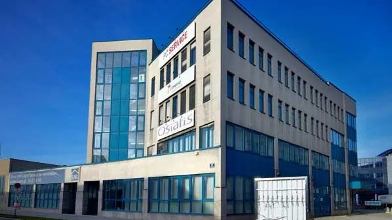 Modernes Bürogebäude mit blauen Fensterrahmen und Glasfassade unter klarem Himmel.