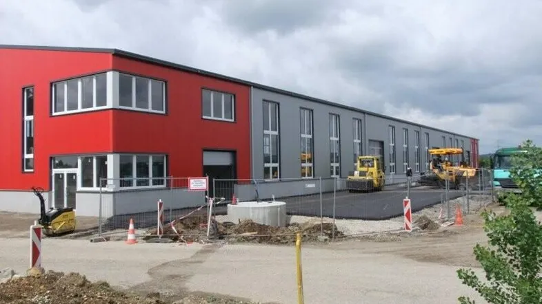 Modernes Geschäftsgebäude mit roter und grauer Fassade, umgeben von einer Baustelle mit Baugeräten und neuem Asphalt.