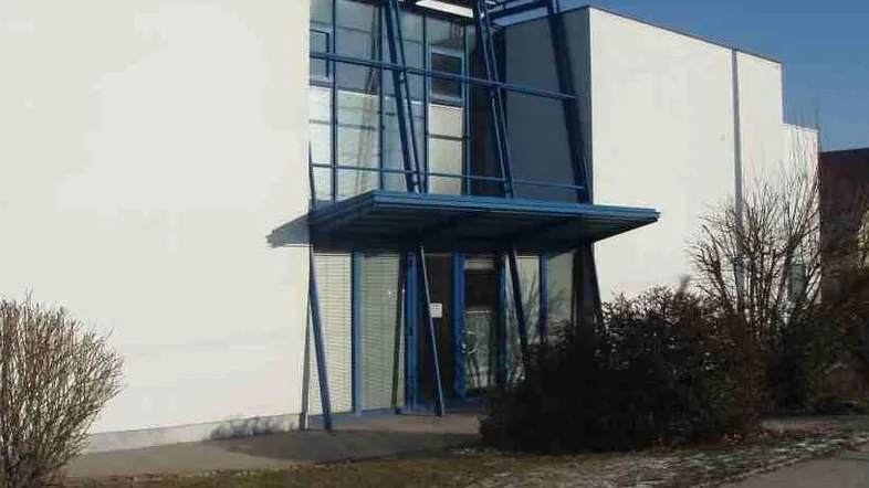 Moderne Gebäudefassade mit markantem blauen Metallrahmen und großflächiger Glasfront am Eingangsbereich.
