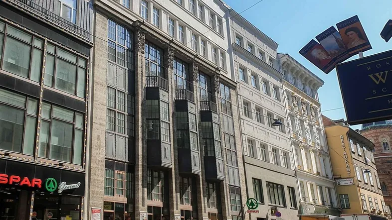 Historische Gebäudefassade mit Geschäften im Erdgeschoss und traditioneller Architektur in einer belebten Straße.